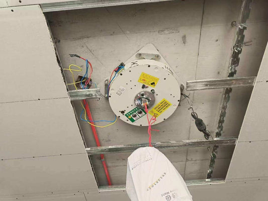 Motorized chandelier lift system installed on a ceiling, showcasing wiring and control components.